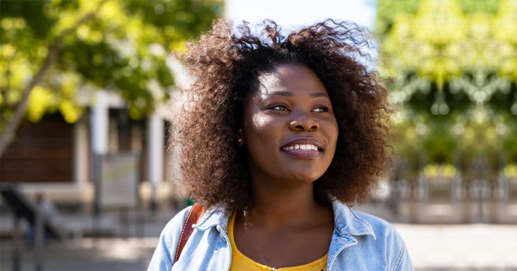 natural haired black woman smiling while looking away onto the street and thinking